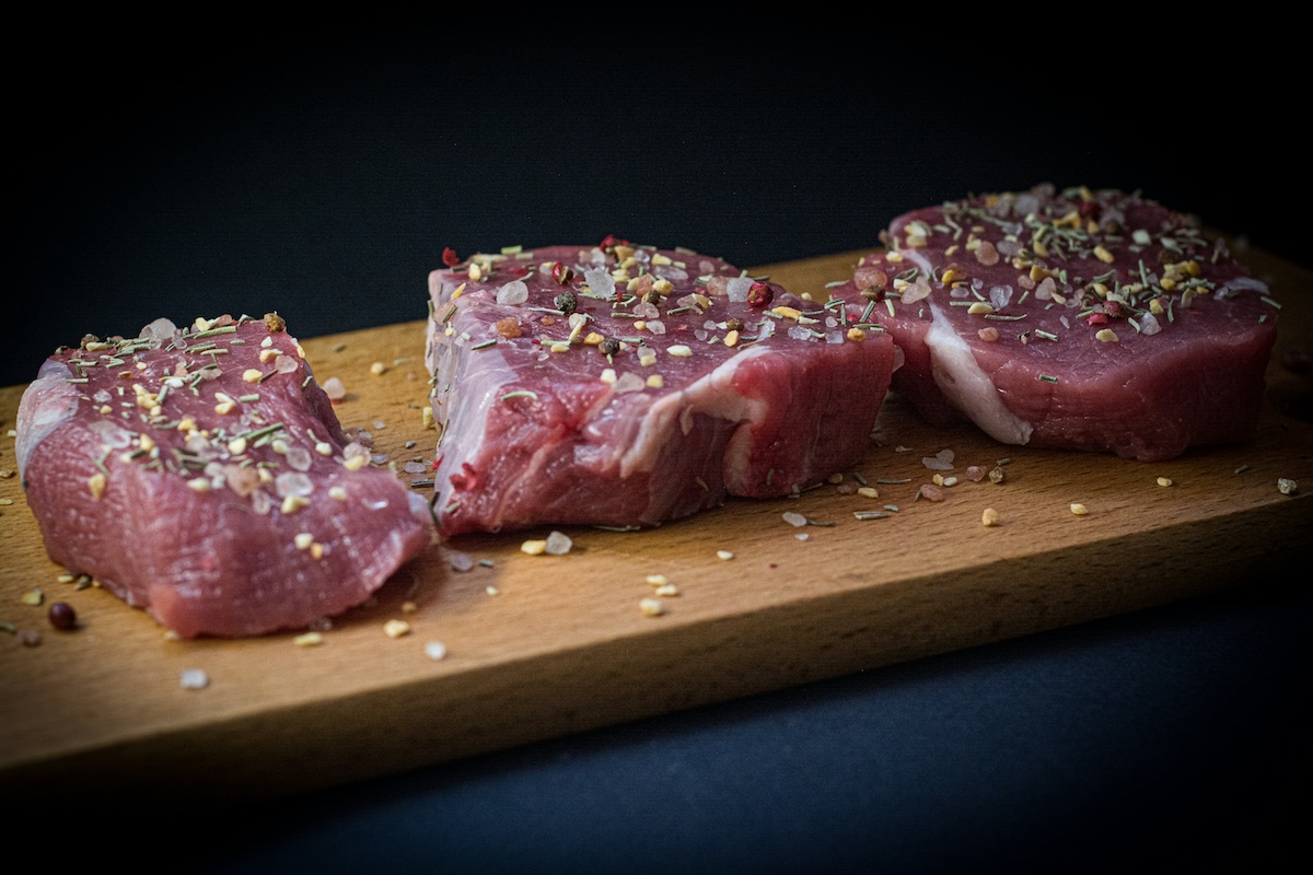 Sazonando unas costillas de cerdo con una mezcla de especias secas de color rojo.⁠