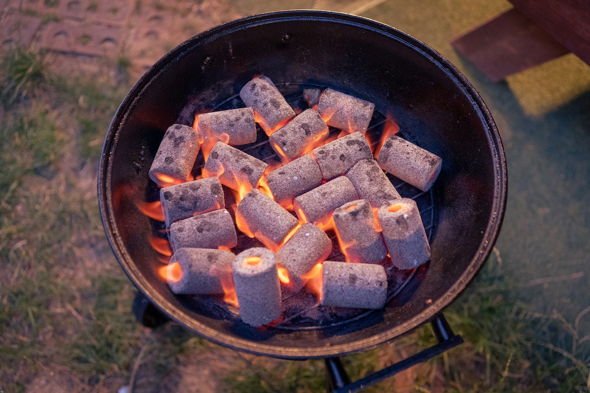 Tacos de leña para ahumar junto a una barbacoa encendida soltando humo.⁠