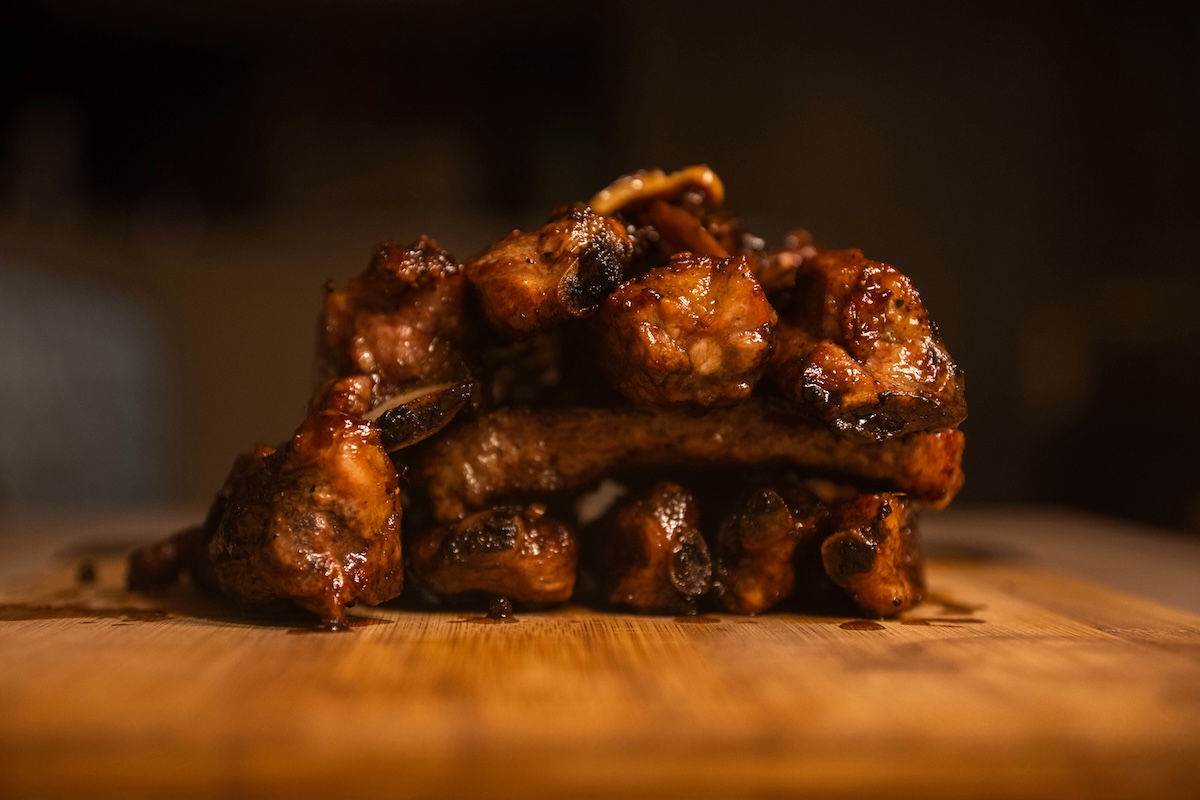 ⁠Un costillar de cerdo ahumado y cortado, brillando con salsa barbacoa caramelizada sobre una tabla.⁠